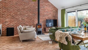 A cozy living room with a brick wall, a fireplace, a sofa, a dining table, and a TV.