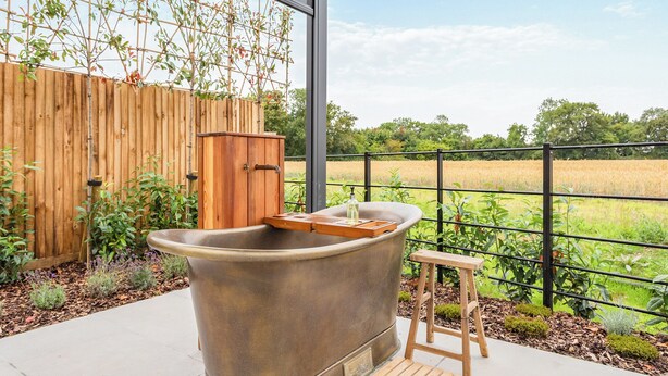 A large outdoor hot tub with a wooden stool, a wooden fence, and a view of a field.