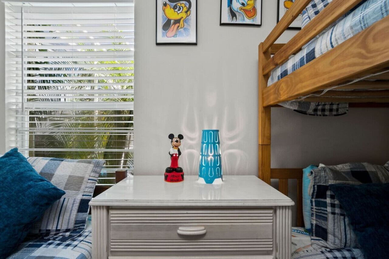 Une chambre d’enfant avec un lit superposé, un bureau orné d’une figurine de Mickey Mouse et une fenêtre avec des stores.