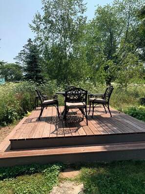 A wooden deck with a table and four chairs, surrounded by greenery and trees. - Our Thunder Moon Farm Stay- sleeps 7, framed by wildflowers. 4 miles to GB. (Oneida)