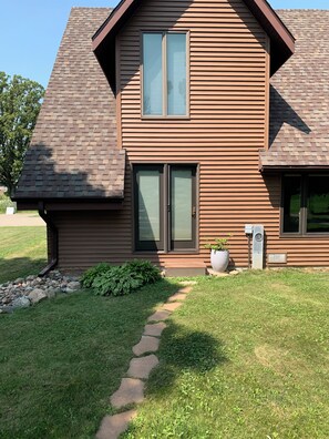 A modern two-story house with a brick roof, a front door with a glass panel, and a small garden area with a stone pathway. - Our Thunder Moon Farm Stay- sleeps 7, framed by wildflowers. 4 miles to GB. (Oneida)