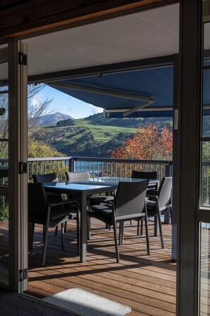 Une terrasse ouverte avec une table et des chaises, offrant une vue panoramique sur un paysage pittoresque composé de collines et d’une étendue d’eau.