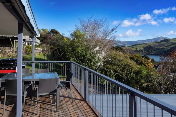 Une terrasse équipée d’un barbecue, de meubles pour s’asseoir à l’extérieur et offrant une vue panoramique sur des collines et un lac.