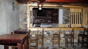 Een bar met stenen muren, een houten toog en verschillende houten stoelen.