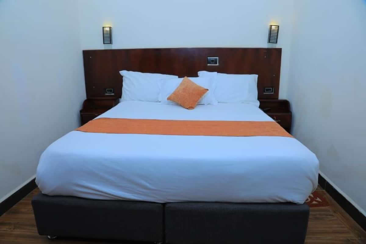 A neatly made bed with white and orange bedding, two bedside tables with lamps, and a dark headboard.