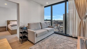 Een moderne hotelkamer met een groot raam, een grijze bank, een houten bed en een klein bijzettafeltje.