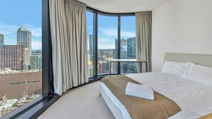 Een moderne hotelkamer met een groot bed, uitzicht op de stad en een gebogen raam met gordijnen.