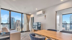 Een moderne woonkamer met een groot raam, een flatscreen televisie, een houten eettafel en een bank.