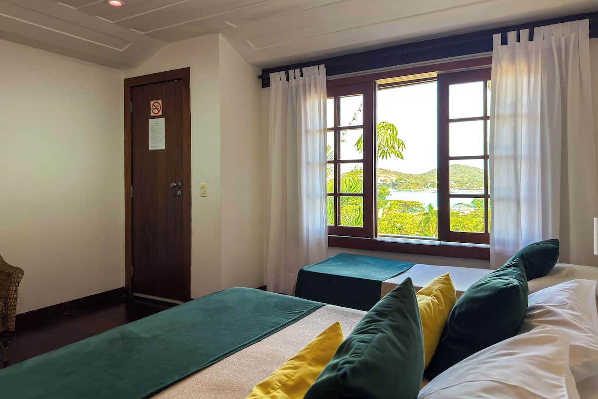 Una habitación con dos camas, una ventana con cortinas, una puerta y vistas al exterior con vegetación.