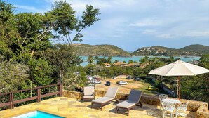 A swimming pool with lounge chairs and umbrellas, surrounded by greenery and overlooking a scenic landscape. - Pousada Encanto de Buzios (Búzios)