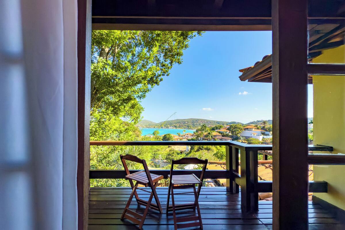 Una terraza de madera con dos sillas y una mesa, con vistas panorámicas a una zona costera con casas y vegetación.