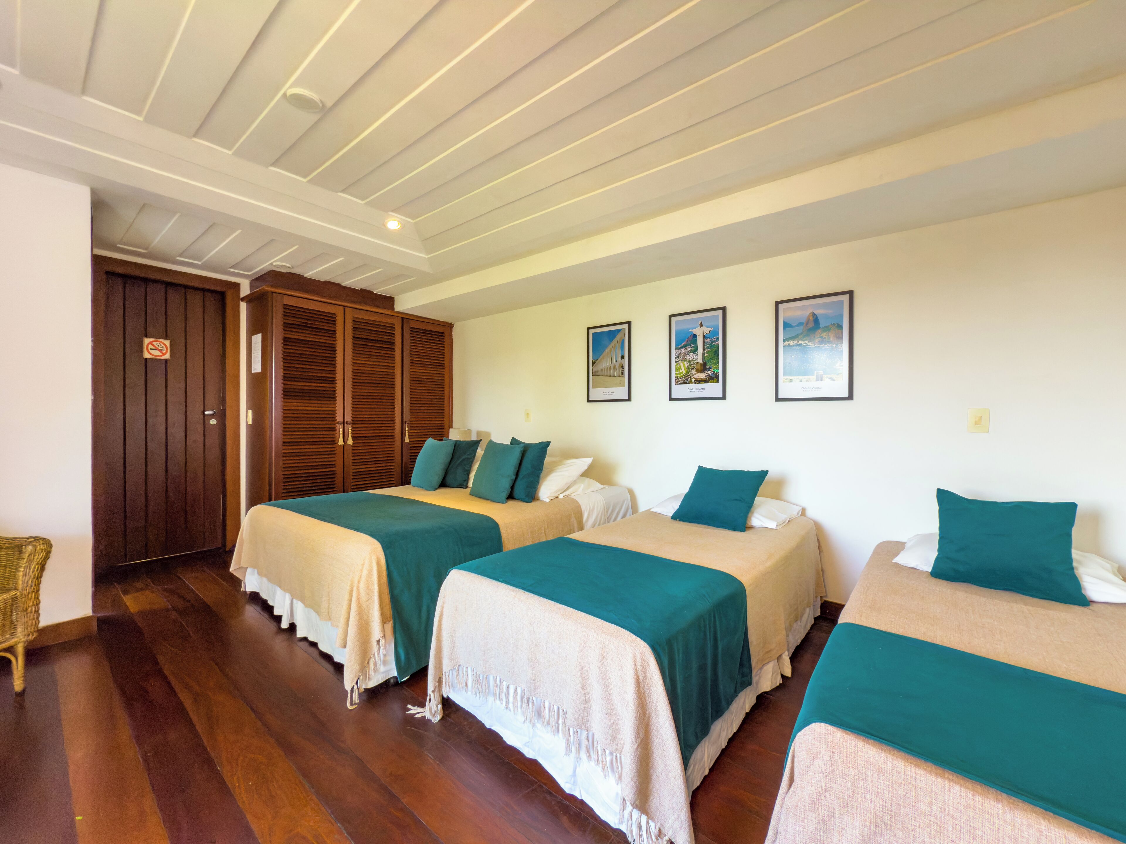 A hotel room with two beds, wooden wardrobe, and three framed pictures on the wall.