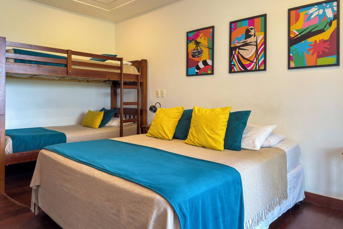 Habitación de hotel con literas, una cama grande con muchas almohadas y coloridas obras de arte en las paredes.