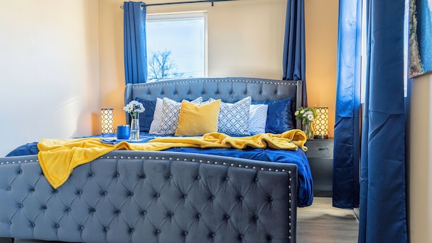 Una cama grande con cabecera capitonada, ropa de cama azul y una manta amarilla.