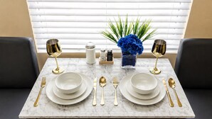 Una mesa de comedor dispuesta con platos blancos, cubiertos dorados y un jarrón con flores azules.