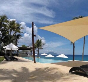 A poolside area with umbrellas, lounge chairs, and palm trees. - Beachfront Condo Airport transport incl (Sosúa)
