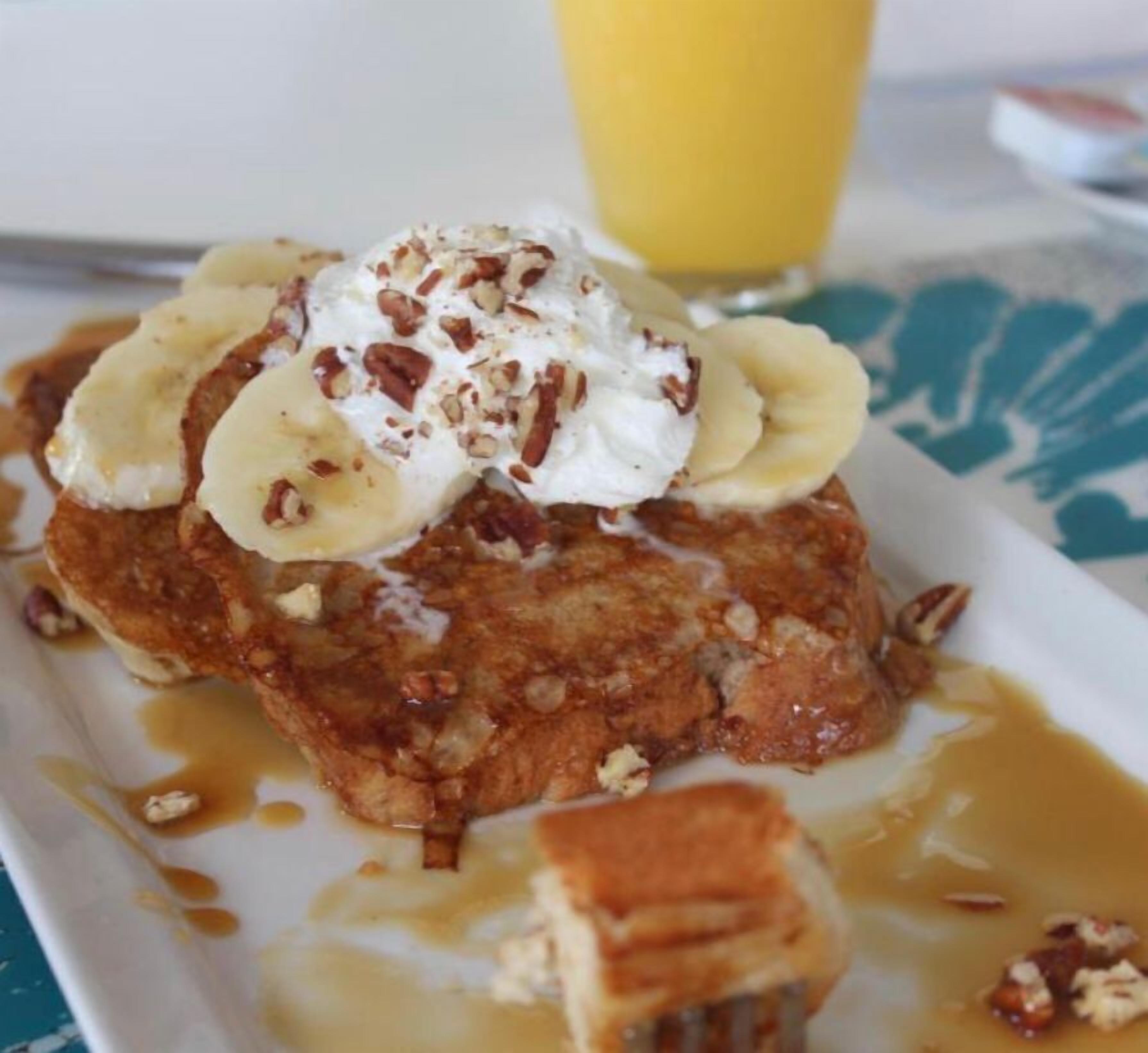 Ein Teller mit Bananenpfannkuchen, bedeckt mit Schlagsahne und Pekannüssen, serviert mit Ahornsirup.