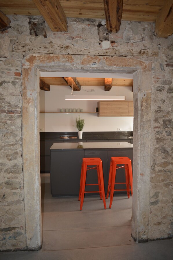 A kitchen with a stone wall, wooden beams, and a modern island with two orange stools.