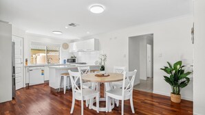 Una cocina moderna con armarios blancos, una mesa de comedor de madera con sillas blancas y una planta en maceta.