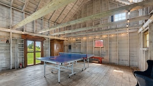 Une table de ping-pong dans une pièce rustique en bois, dotée d’un plafond haut et baignée de lumière naturelle.