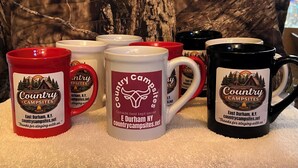 A collection of mugs with 'Country Campsites' branding, featuring a mountain and tent design, placed on a white surface with a tree in the background. - Delightful Apartment in the Mountains East Durham with AC, Dogs Friendly 2 max  (East durham)