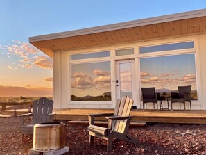 A modern building with large windows, a wooden deck, and outdoor seating.