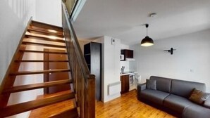 Un escalier mène à un espace de vie comprenant un canapé et, au fond, une cuisine.