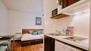 Une chambre d’hôtel de taille réduite comprenant un lit, une petite kitchenette et un coin repas.