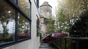 Un bâtiment moderne doté de grandes fenêtres et d’une tour en pierre en arrière-plan.