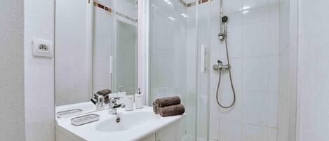 A modern bathroom with a white sink, mirror, and glass-enclosed shower.