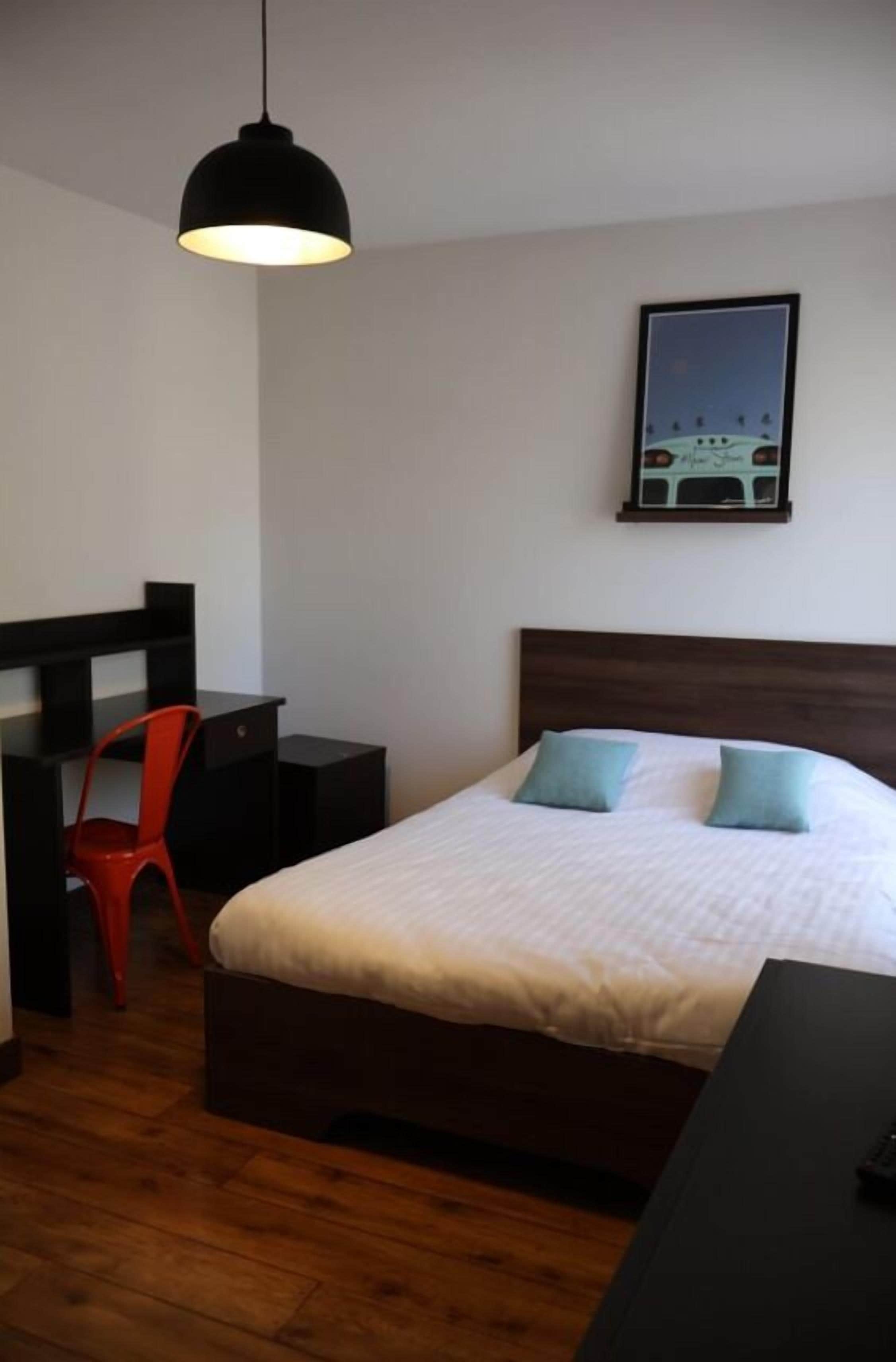 A bedroom with a bed, a desk, a chair, and a hanging light fixture.