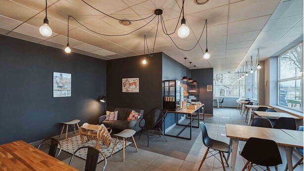 Un café moderne avec des tables et des chaises en bois, un canapé noir et des luminaires suspendus.