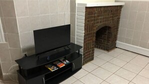 A living room with a flat-screen TV on a black stand, a fireplace, and a tiled floor. - Private 1-bedroom apartment, 15 minutes to Manhattan, NYC bus at the door (Union City)