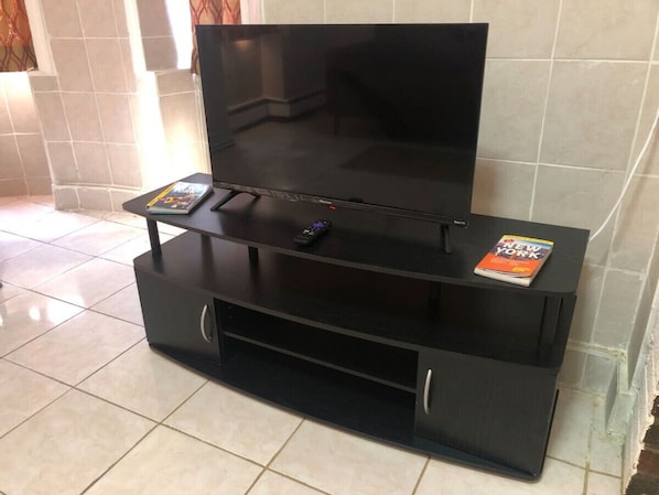Un meuble noir pour appareils électroniques, avec un téléviseur à écran plat, une télécommande et un magazine posé sur le dessus.
