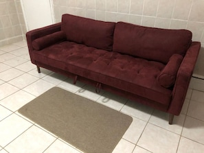 En vinrød sofa med tilhørende gulvtæppe på flisegulv.