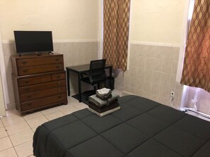 Une chambre à coucher comprenant un lit, une commode, un bureau, une chaise et un téléviseur.