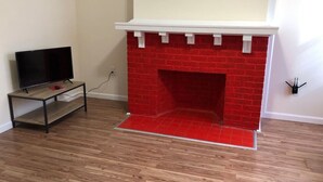 A room with a red brick fireplace, a television on a stand, and a wooden floor. - Private 3 bed, 1 bath apartment near EWR/NYC (Newark)