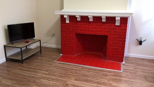 Una habitación con chimenea de ladrillo rojo, un televisor sobre un mueble bajo y piso de madera.