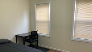Un dormitorio con una cama, un escritorio y dos ventanas con persianas.