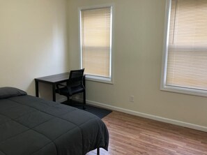A bedroom with a bed, a desk, and two windows with blinds.