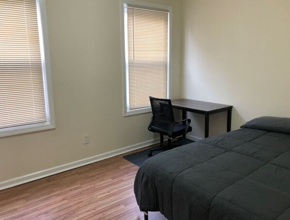 A bedroom with a bed, a desk, and two windows with blinds.