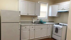 Cocina compacta con alacenas blancas, refrigerador, estufa y ventana con persianas.