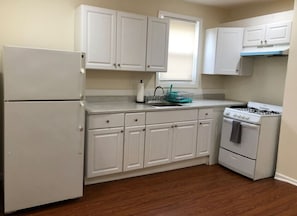 A compact kitchen with white cabinets, a refrigerator, a stove, and a window with blinds.