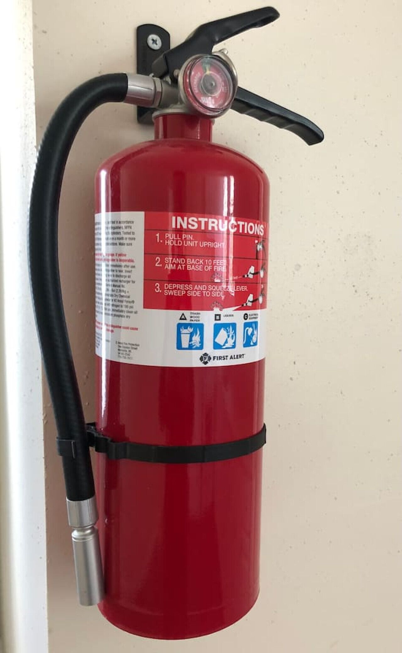 A red fire extinguisher mounted on a wall with instructions and safety symbols.