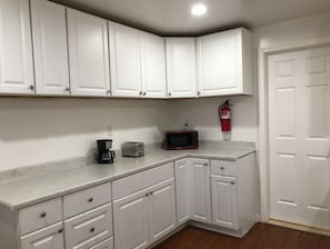 Una cocina con gabinetes blancos, microondas, tostadora y cafetera.
