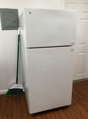 Ein weißer Kühlschrank in einem Raum mit Holzboden und einem an der Wand angelehnten Besen.