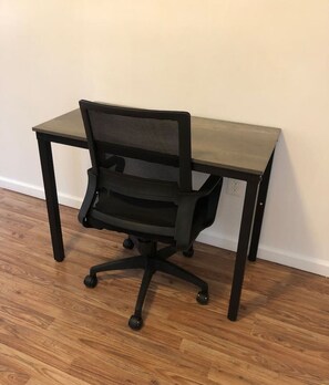 Ein schwarzer Bürostuhl mit atmungsaktivem Netzrücken und Rollen steht auf Holzdielen neben einem dunklen Schreibtisch.