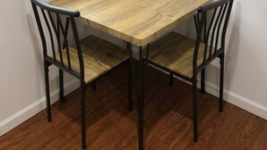 Een hoekige eethoek met een houten tafel en vier stoelen, een raam met zonwering, en een houten vloer.