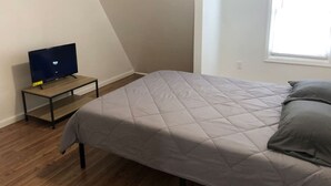 Een slaapkamer met een bed, een televisie op een tafeltje en een raam.