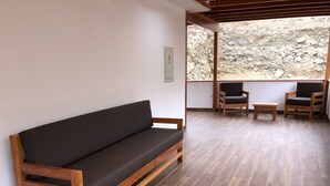 A wooden sofa with a dark cushion in a room with wooden flooring and a view of rocky terrain through a large window.